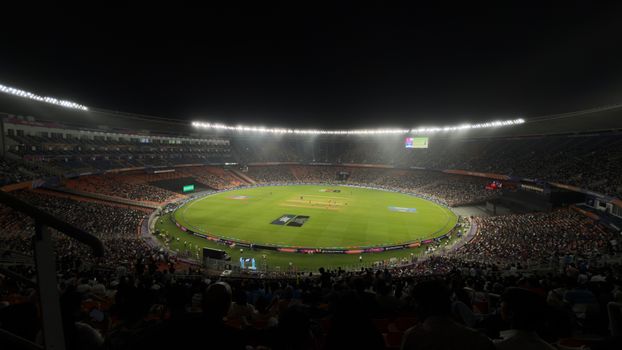 Spelers in een vol cricketstadion tijdens een IPL-wedstrijd onder avondlicht